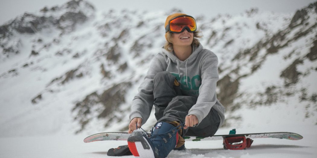 Mężczyzna zawiązujący na stoku buty snowboardowe