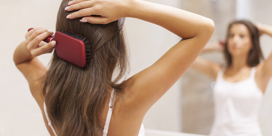 Kobieta przed lustrem czesząca włosy szczotką