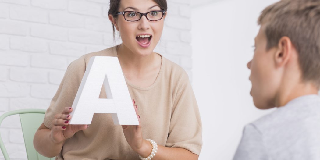 kobieta z białą literą A na zajęciach z logopedii z chłopcem