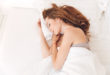 uśmiechnięta rudowłosa kobieta śpiąca w łóżku w białej pościeli