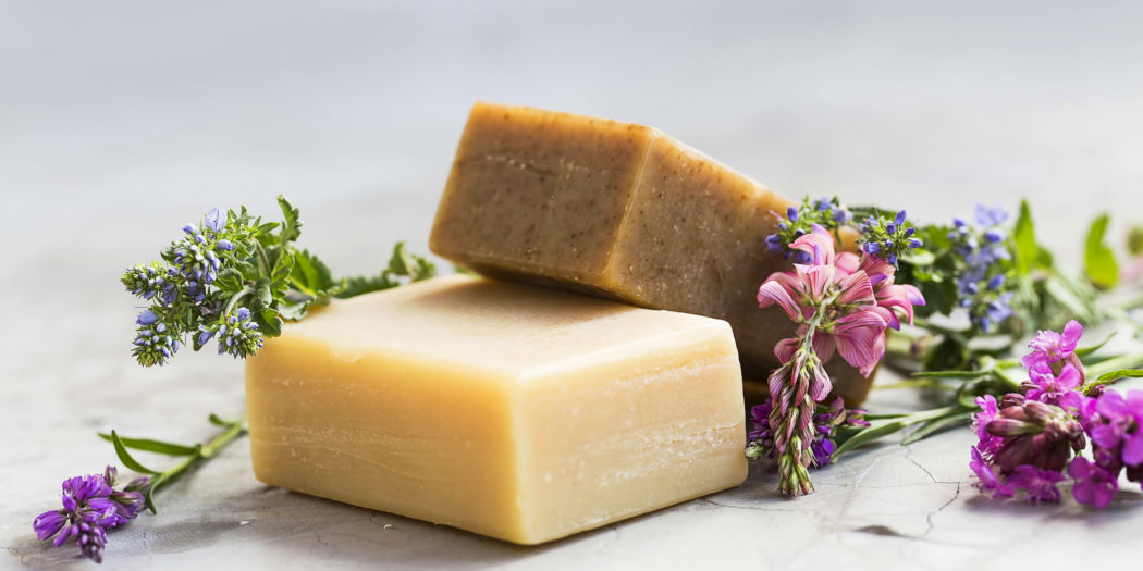 kostki naturalnych mydeł obok ziół i kwiatów